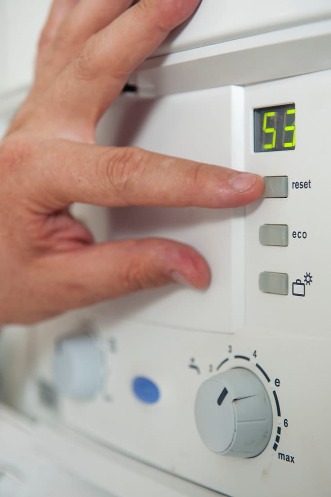A finger pressing the reset button on a white control panel