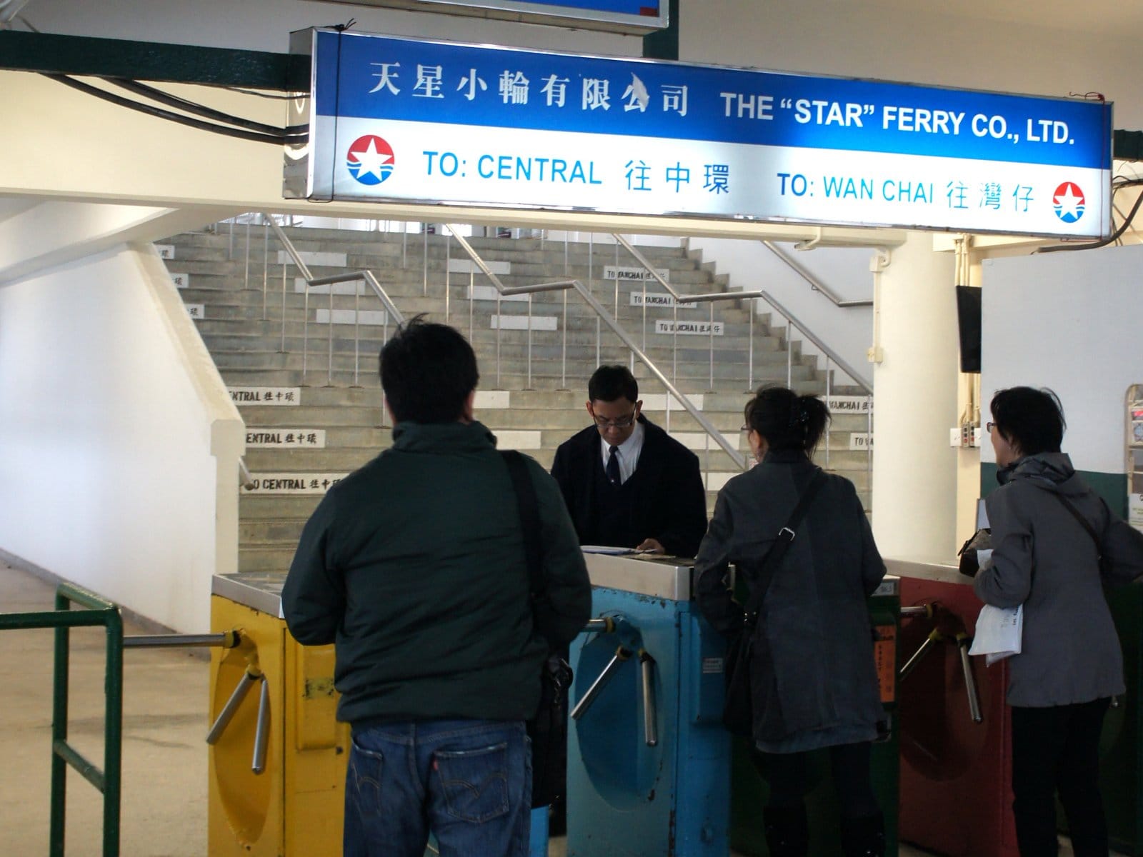 Passengers waiting at a row of turnstiles while an attendant checks something at the gate before letting them through