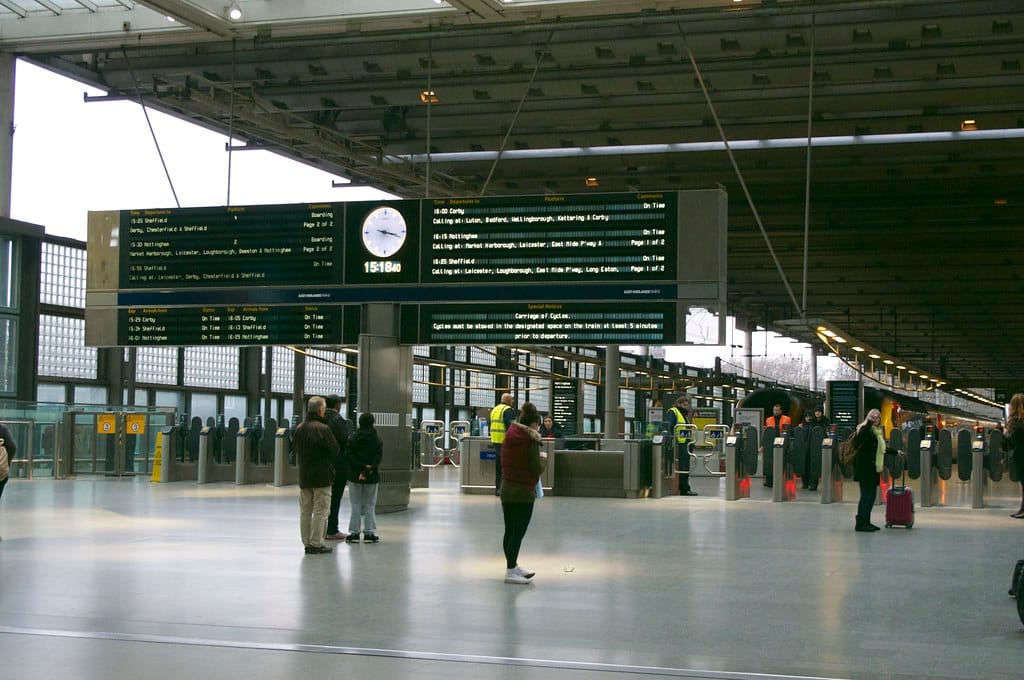 Departure boards and a station clock above the ticket gates in a large railway concourse